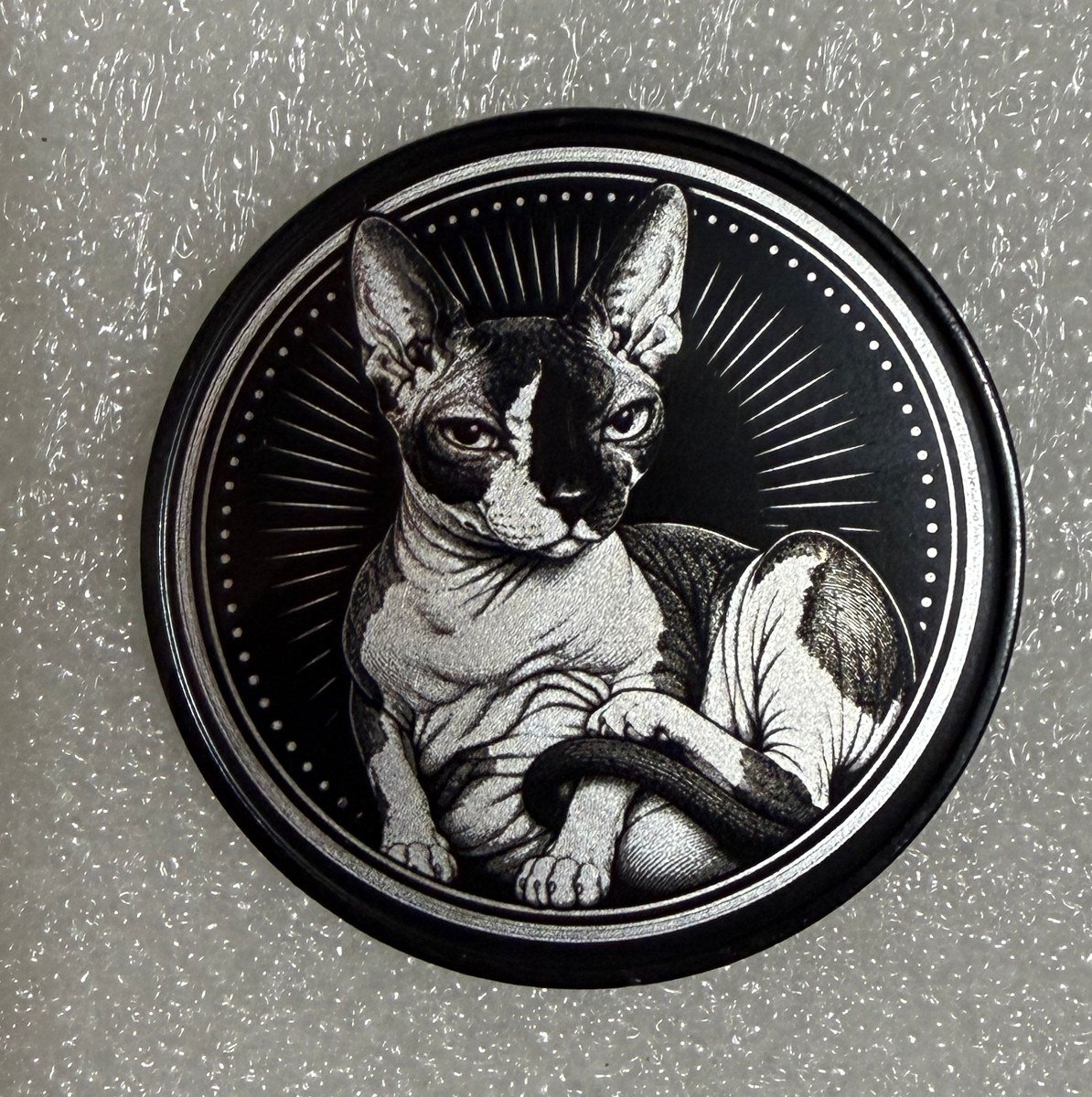 Front of an anodized steel coin with a detailed cat engraving