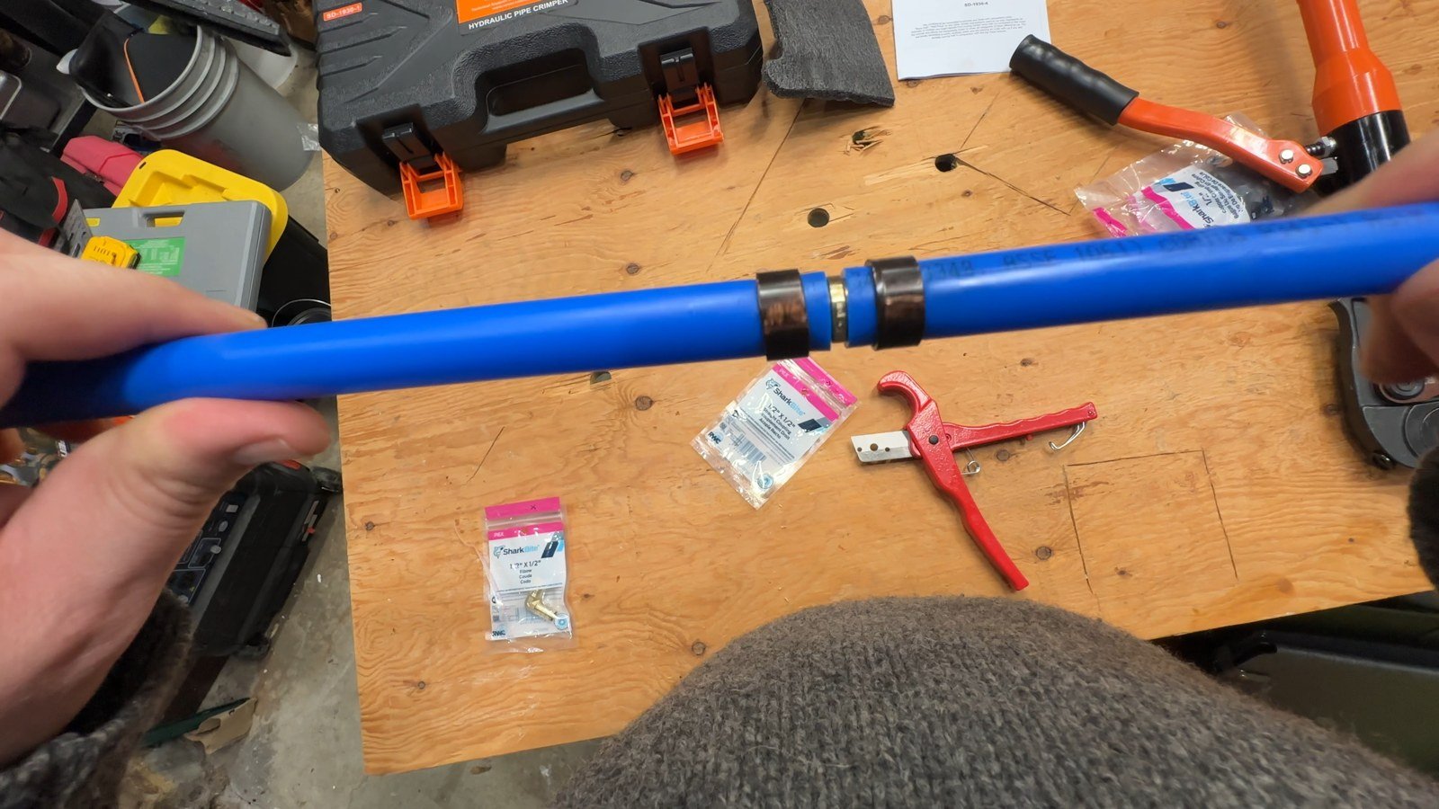 Two blue PEX sections joined by a barbed coupling with copper crimp rings after the demonstration